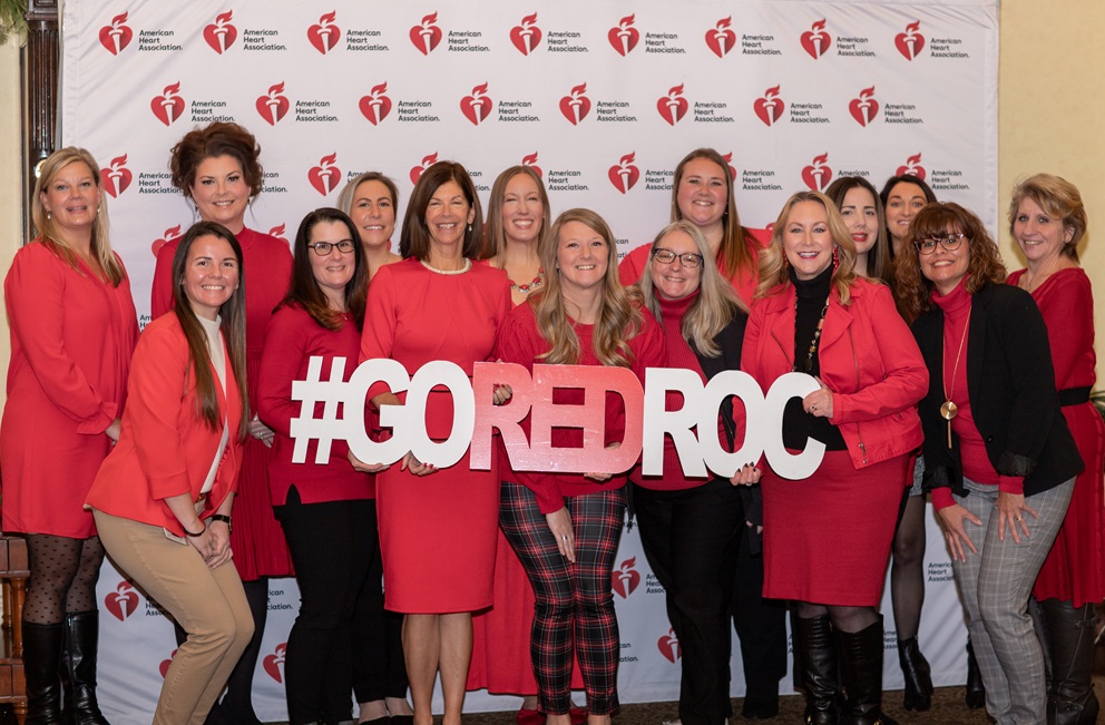 Large group of women in red holding sign reading hashtag go red roc